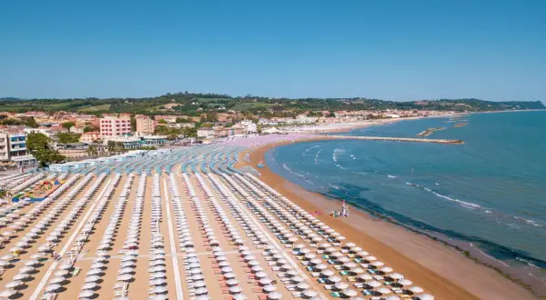 Fano mare: file ordinate di ombrelloni bianchi e colorati sulla sabbia dorata, con il mare azzurro e la costa sullo sfondo.