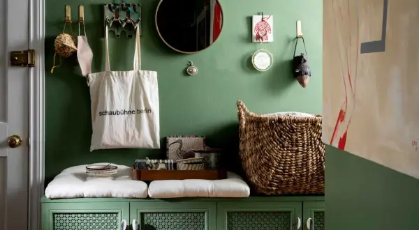 Charming apartment entryway ideas: green cabinet with cushions, tote bag, mirror, and woven basket.