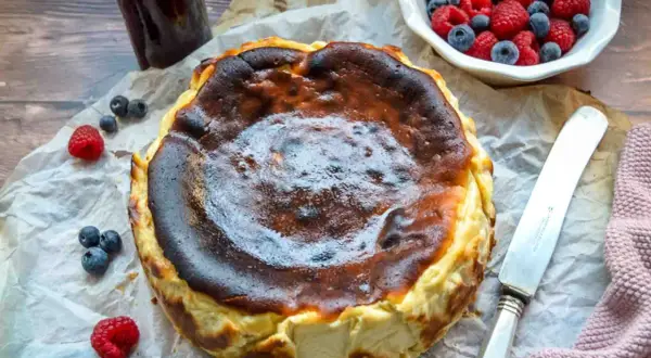 Ein perfekt gebackener San Sebastian Cheesecake mit karamellisierter Kruste, garniert mit frischen Beeren und einem Glas Marmelade.