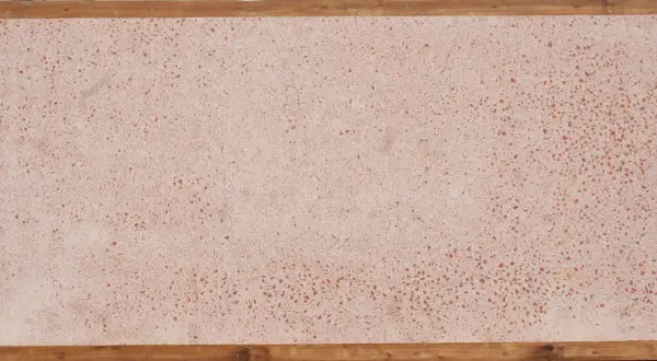 Superficie in coccio pesto con venature rosse, incorniciata da listelli di legno grezzo.