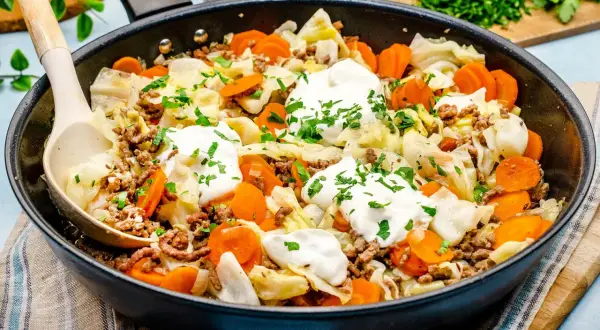 Herzhaftes spitzkohl mit hackfleisch in der Pfanne, garniert mit Klecksen saurer Sahne und Petersilie. Ein deftiges Gericht!