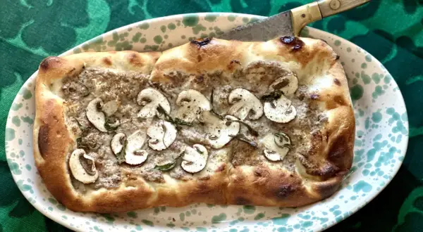 En gyllene pinsa med svamp och örter, redo att skäras med en kniv. Ett perfekt pinsa recept för en mysig kväll.