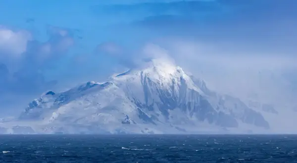 Majestuosa montaña nevada emerge de las aguas agitadas, un paisaje que evoca el temido paso de Drake.