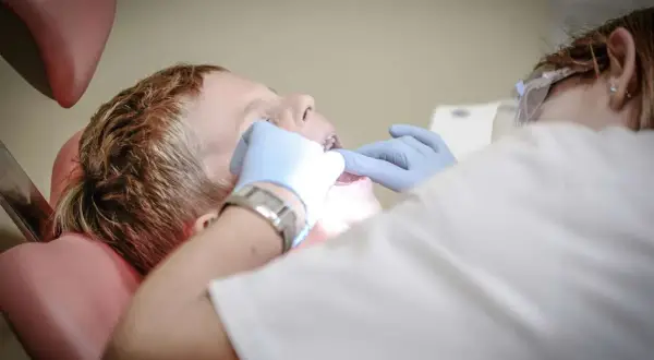 Chłopiec u dentysty, który bada jego usta. Może to być spowodowane bólem podniebienia przy zębach górnych.