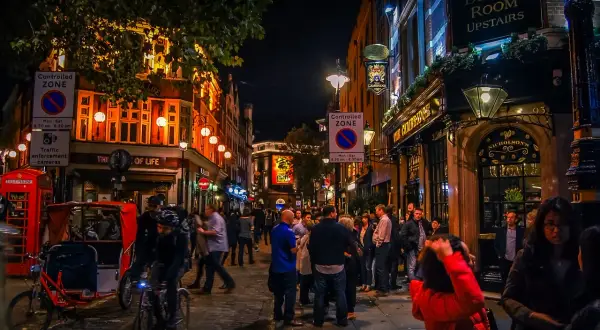 En livlig gata i London på kvällen, med folk som minglar utanför pubar och restauranger, som påminner om stadens nattklubbar.