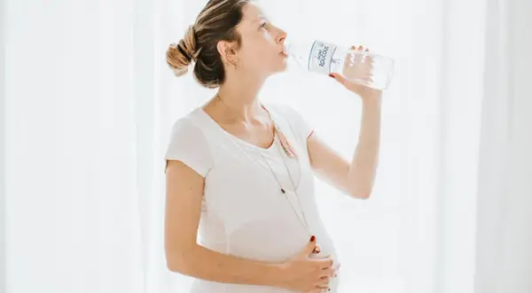 Une femme enceinte boit de l'eau d'une bouteille, prenant soin de son hydratation.