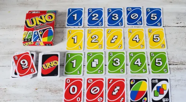 Karty UNO ułożone w rzędy. Widać pudełko i karty z cyframi 0-5 w kolorach niebieskim, żółtym, zielonym i czerwonym. Czy można kłaść kilka kart?