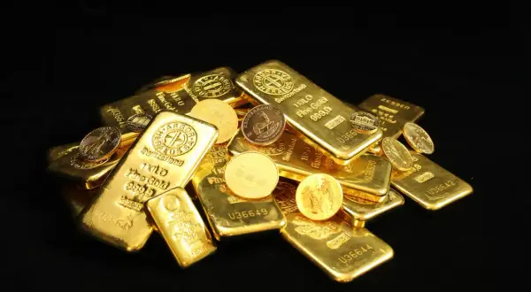 Złote sztabki i monety, w tym słynny Krugerrand, błyszczą na czarnym tle.