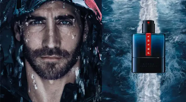 Mężczyzna z kroplami wody na twarzy obok butelki perfum Prada Luna Rossa Ocean.