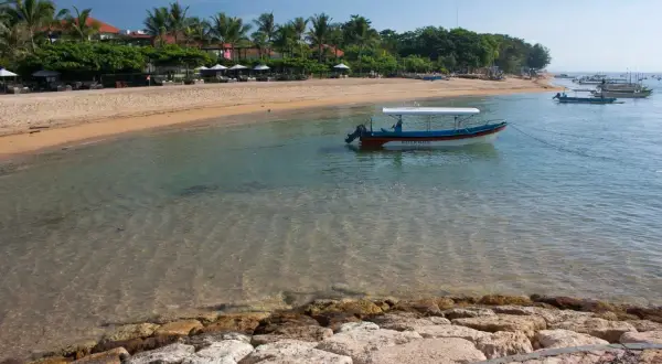 Spokojna plaża w Sanur z łodzią "Water Walk" kołyszącą się na turkusowej wodzie.