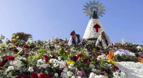 Ofrenda de flores a la Virgen del Pilar. Hombres colocan flores en una estructura adornada con la imagen de la Virgen.