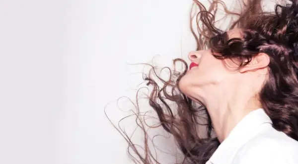 Frauenkopf mit wallenden, braunen Locken, die sich im Wind bewegen. Tipps, wie man locken richtig pflegt, um diesen Schwung zu erhalten.