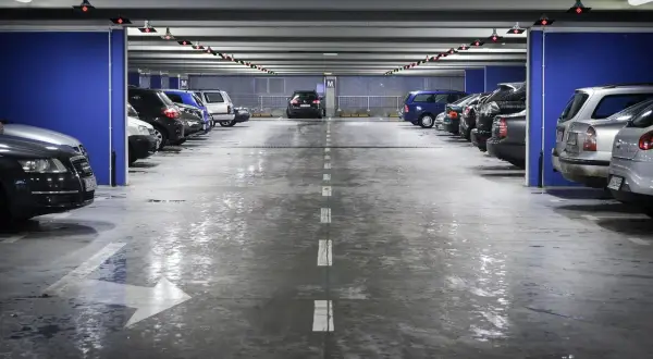 Wielopoziomowy plac postojowy, gdzie mokra podłoga parkingu odbija światła.