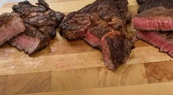 Tre saftiga steak minute-biffar, perfekt stekta med rosa kärna, ligger på en träskärbräda.
