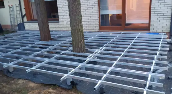 Trwa układanie deski kompozytowej na aluminiowym stelażu, który omija drzewa rosnące na tarasie.