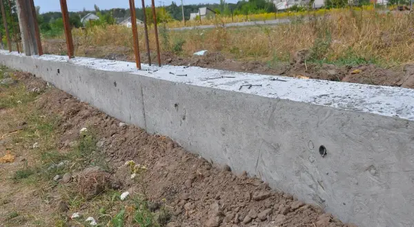 Trwa montaż paneli ogrodzeniowych do starych słupków. Wylano betonowy fundament, w którym osadzono zbrojenie.