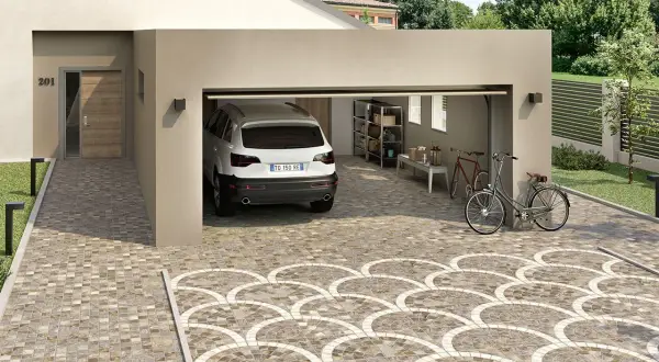 Un'auto bianca è parcheggiata in un garage aperto. Il vialetto carrabile del giardino è pavimentato con piastrelle decorative a ventaglio.