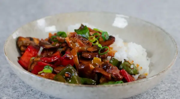 En skål med ris och en smakrik kyckling cashew-röra med paprika och svamp, toppad med salladslök.