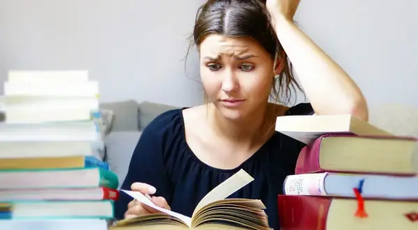 Joven con libros apilados, pensativa, buscando qué hacer cuando te aburres.
