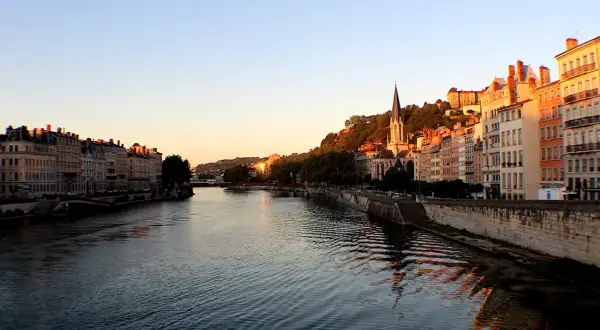 Vue de Lyon au coucher du soleil, avec le Rhône et ses quais bordés d'immeubles. La descente du Rhône offre un spectacle paisible.