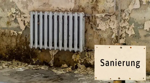 Altes Heizkörper, Wand bröckelt, ein Schild mit "Sanierung" weist auf den Zustand hin. Es ist offensichtlich, dass hier etwas leck und undicht ist.