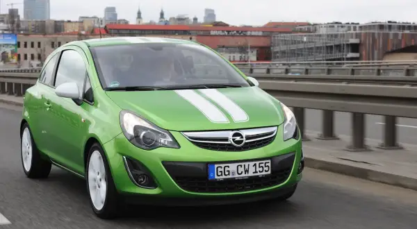 Zielony Opel Corsa D z białymi pasami na masce, z nowymi żarówkami w reflektorach, jedzie po moście.