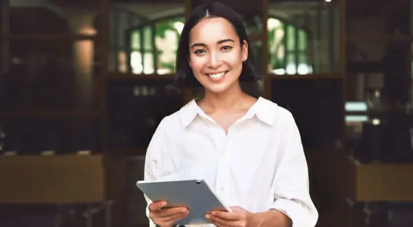 Junge Frau mit Tablet lächelt. Sie plant ihr Eventmanagement Studium dual und ist bereit für neue Herausforderungen.