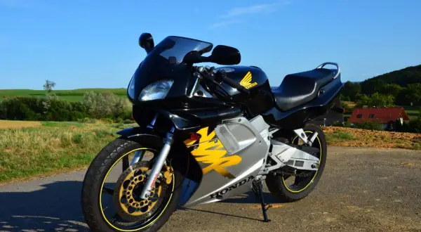 Czarny motocykl Honda NSR z żółtymi akcentami na tle zielonych pól i błękitnego nieba.