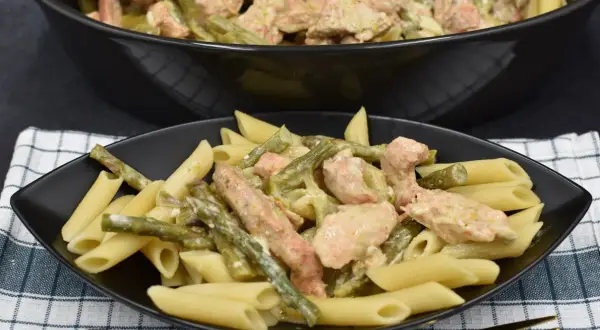 Penne z kurczakiem i szparagami w kremowym sosie. Pyszne danie na talerzu i w garnku.