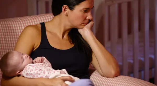Eine Frau sitzt nachdenklich mit ihrem Baby im Arm. Die Szene deutet auf postnatale Depression hin, eine schwere Zeit für viele Mütter.