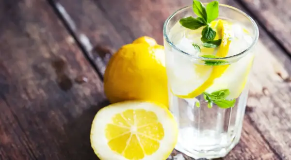Erfrischendes zitronen wasser mit Eis und Minze, daneben ganze und halbierte Zitronen auf rustikalem Holz.