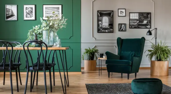Elegancki salon z dominującym kolorem ścian butelkowa zieleń. Wygodny fotel i puf w tym samym odcieniu.