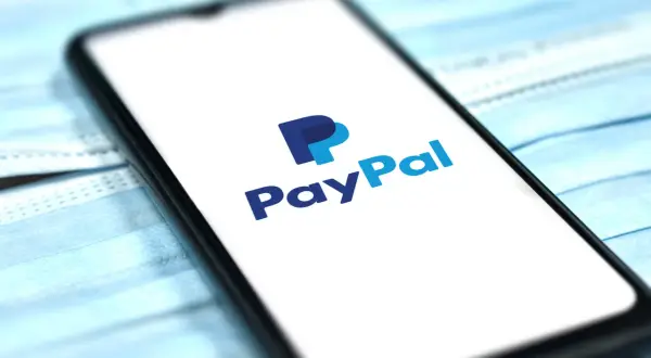 Telefon z logo PayPal na ekranie, leżący na niebieskich maseczkach. Chcesz wiedzieć, jak usunąć PayPal?