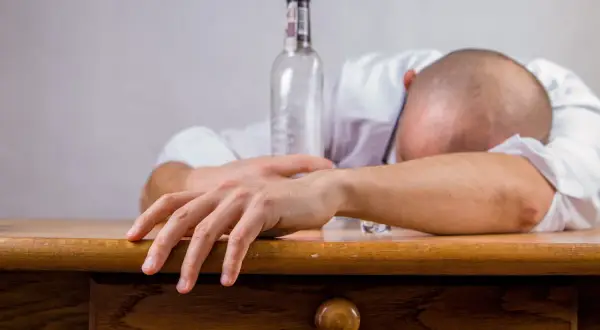Mężczyzna śpi na stole obok pustej butelki. To obraz symbolizujący trudne fazy trzeźwienia i walkę z nałogiem.