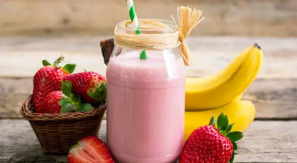Pyszny koktajl truskawkowo bananowy w słoiku, obok świeże owoce i słomka. Idealny na orzeźwienie!