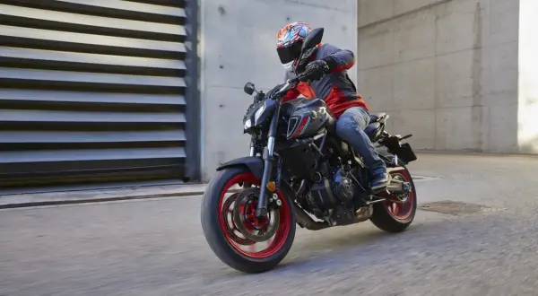 Motociclista con casco y chaqueta roja y gris conduce una Yamaha MT-07 negra con detalles rojos por una calle urbana.
