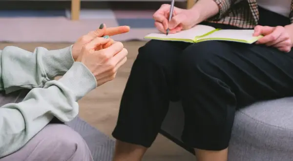 Dwie osoby rozmawiają o uzależnieniach behawioralnych. Jedna wskazuje palcem, druga notuje.