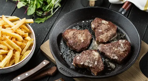 Stekta oxfilébitar i gjutjärnspanna med pommes frites och sallad. Ett perfekt oxfile recept för en lyxig middag.