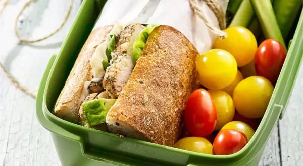 Pyszna kanapka z kurczakiem, świeże pomidorki i ogórek w zielonym pudełku na lunch.