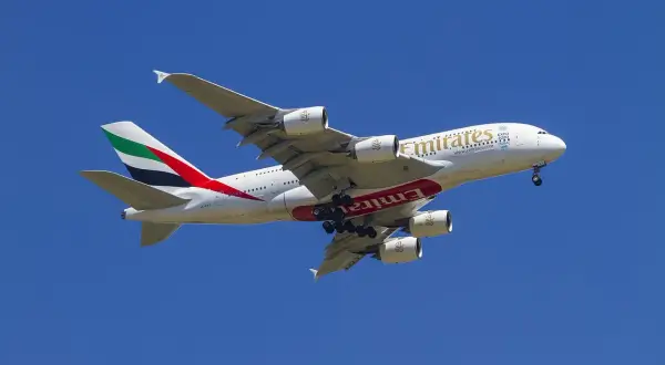 Ogromny samolot Emirates z wysuniętym podwoziem, gotowy do lądowania. Idealny do przewozu bagażu podręcznego.
