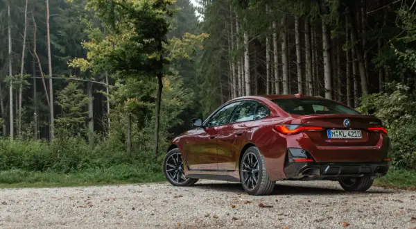 Ciemnoczerwone BMW Gran Coupé na szutrowej drodze w lesie.