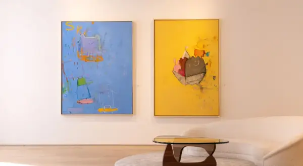 Two vibrant paintings, showcasing playful figures and abstract elements, exemplify modern art trends. A plush sofa and unique coffee table complete the stylish scene.
