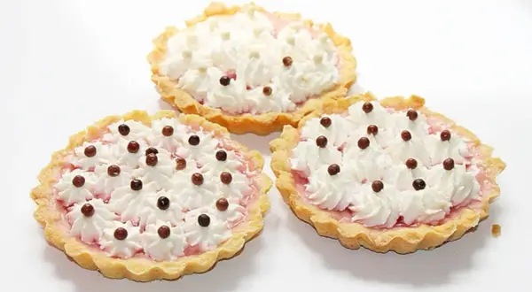 Trzy apetyczne tartaletki z owocami i galaretką, ozdobione bitą śmietaną i czekoladowymi kuleczkami.