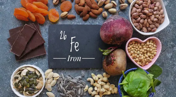 Una tavola ricca di alimenti ricchi di ferro: cioccolato fondente, albicocche, mandorle, pistacchi, barbabietole, fagioli, soia, spinaci, semi di zucca e girasole.