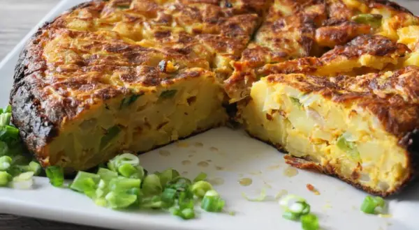 Pyszna tortilla de patatas, pokrojona na kawałki, z zieloną cebulką na talerzu.