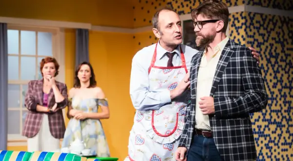 Na scenie "Mayday och teatr" mężczyzna w fartuszku z gęśmi namawia kolegę w kratę. W tle panie.