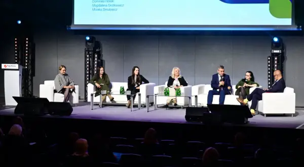 Panel dyskusyjny z udziałem ekspertów na scenie, siedzących na białych sofach.