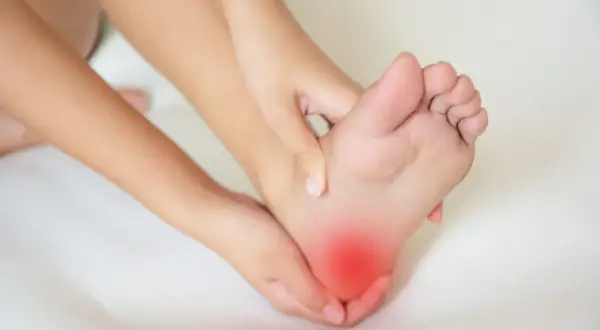 Douleur vive sous le talon, signe d'une possible tendinite sous le pied. Les mains massent la zone rouge.