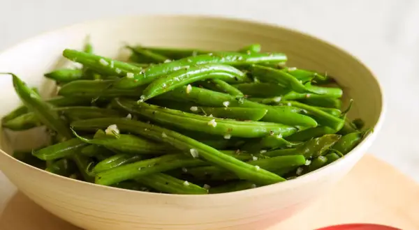 Fagiolini freschi saltati in padella con aglio e pepe, serviti in una ciotola di legno.