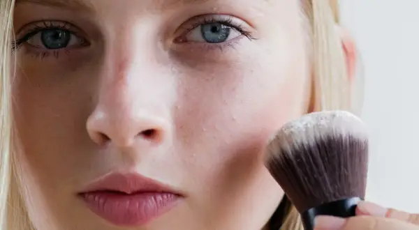 Blondynka nakłada puder transparentny pędzlem. To sekret naturalnego wykończenia makijażu.